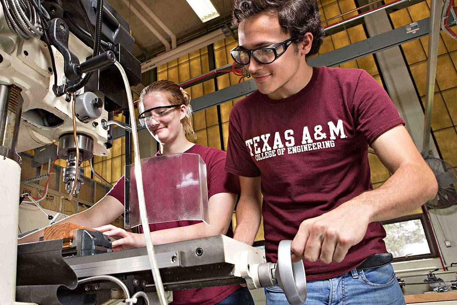 Two engineering students work on heavy machinery while wearing protective goggles
