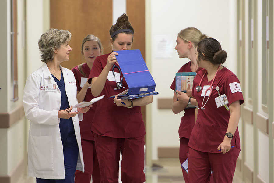 A group of nursing students in maroon scrubs walk down a hallway